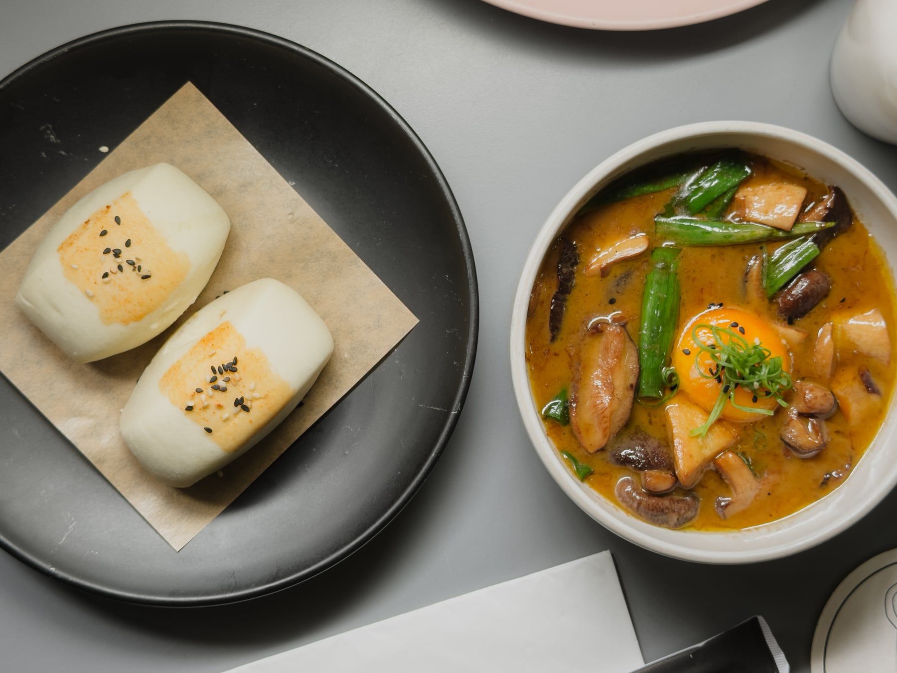 Dois pães bao no vapor ao lado de uma tigela de curry com vagem e cogumelos.