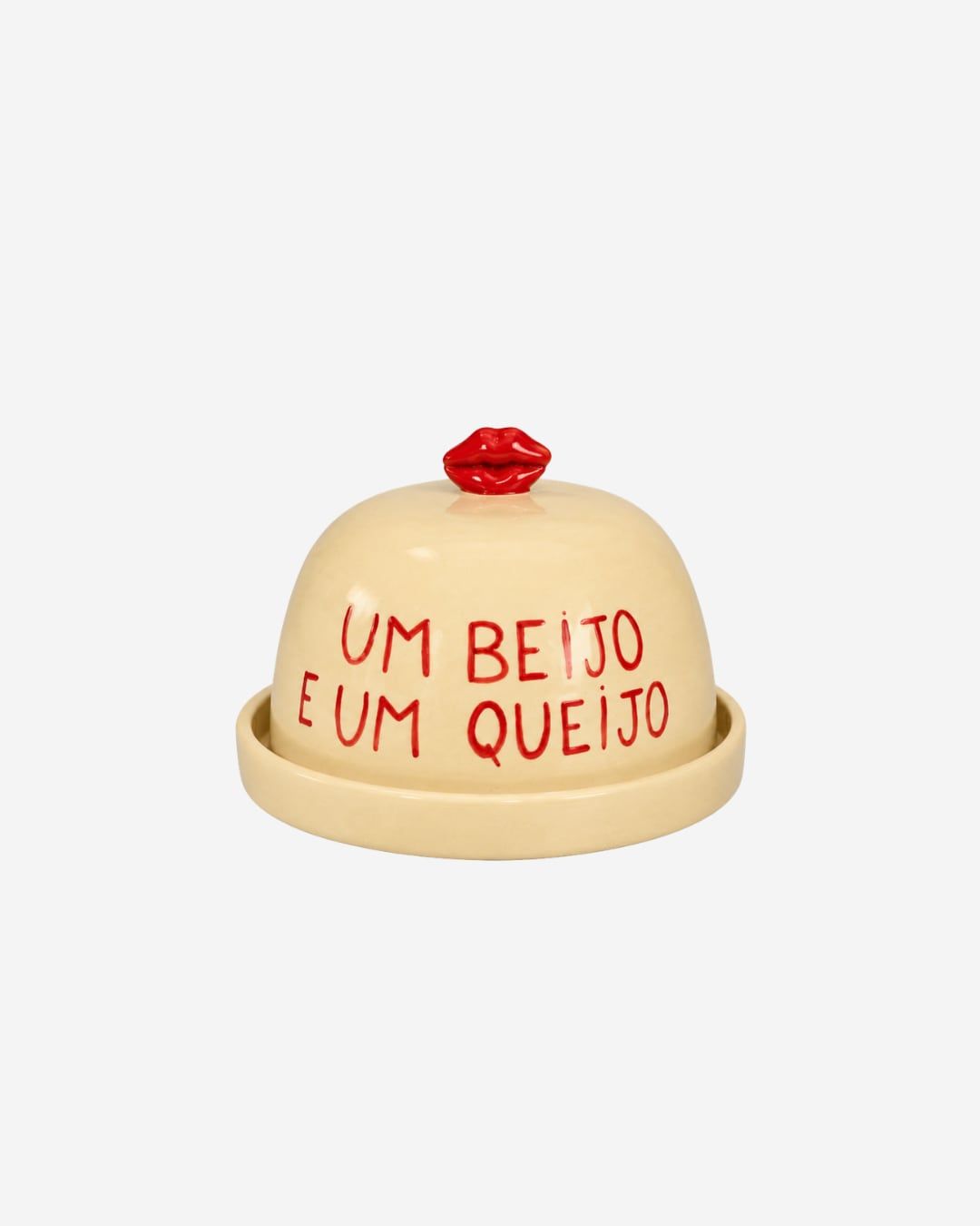 Queijeira de cerâmica creme com tampa escrita à mão “Um beijo e um queijo” e puxador em forma de boca vermelha.