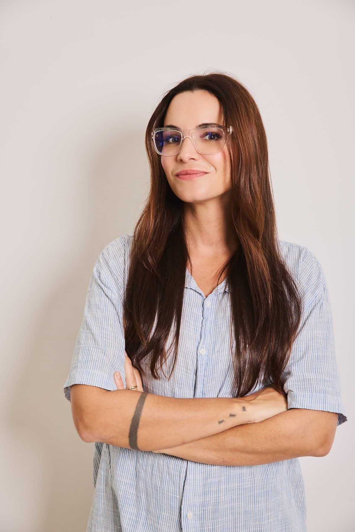 Renata Vanzetto de camisa azul clara e braços cruzados, sorrindo