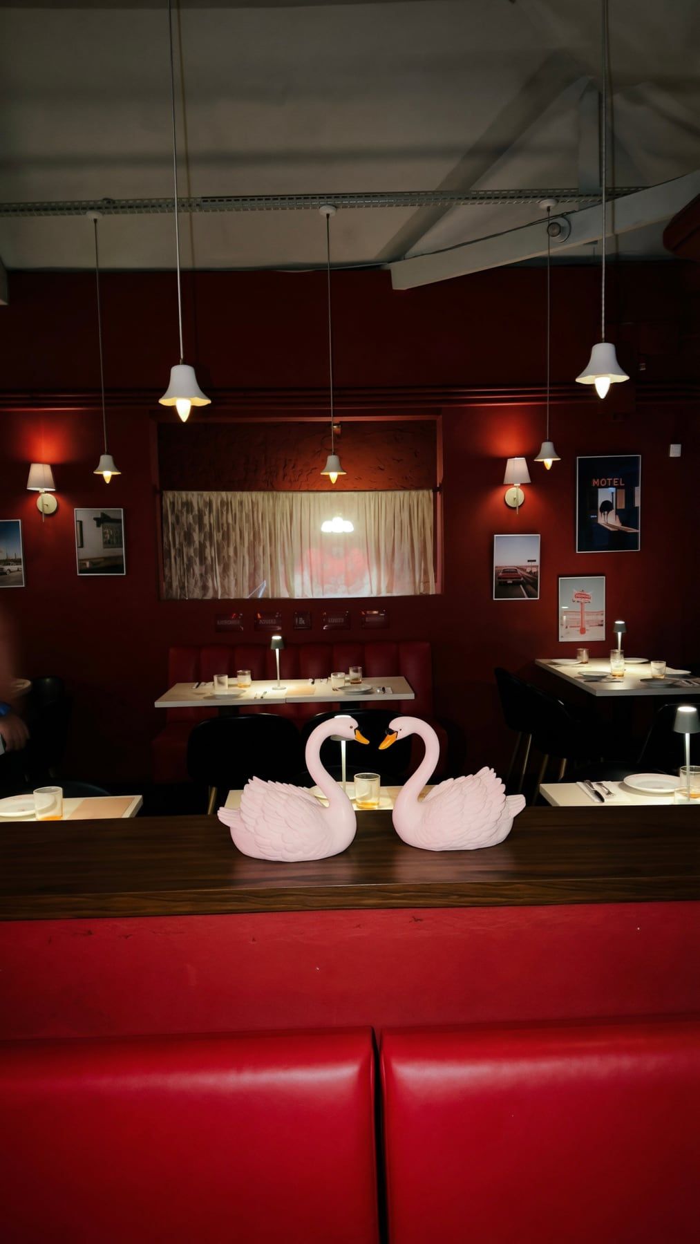 O salão do Motel: paredes e bancos de vinil vermelhos, luminárias penduradas, quadros retrô e dois cisnes cor-de-rosa sobre o balcão.