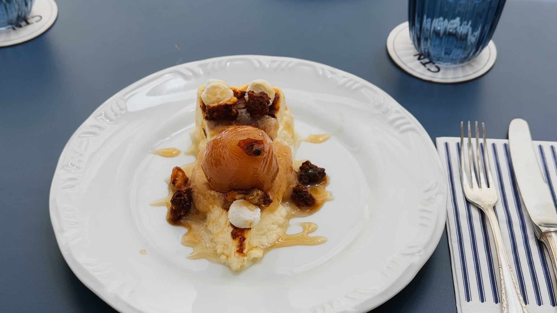 Sobremesa de pera inteira cozida com creme e castanhas caramelizadas, num prato branco.