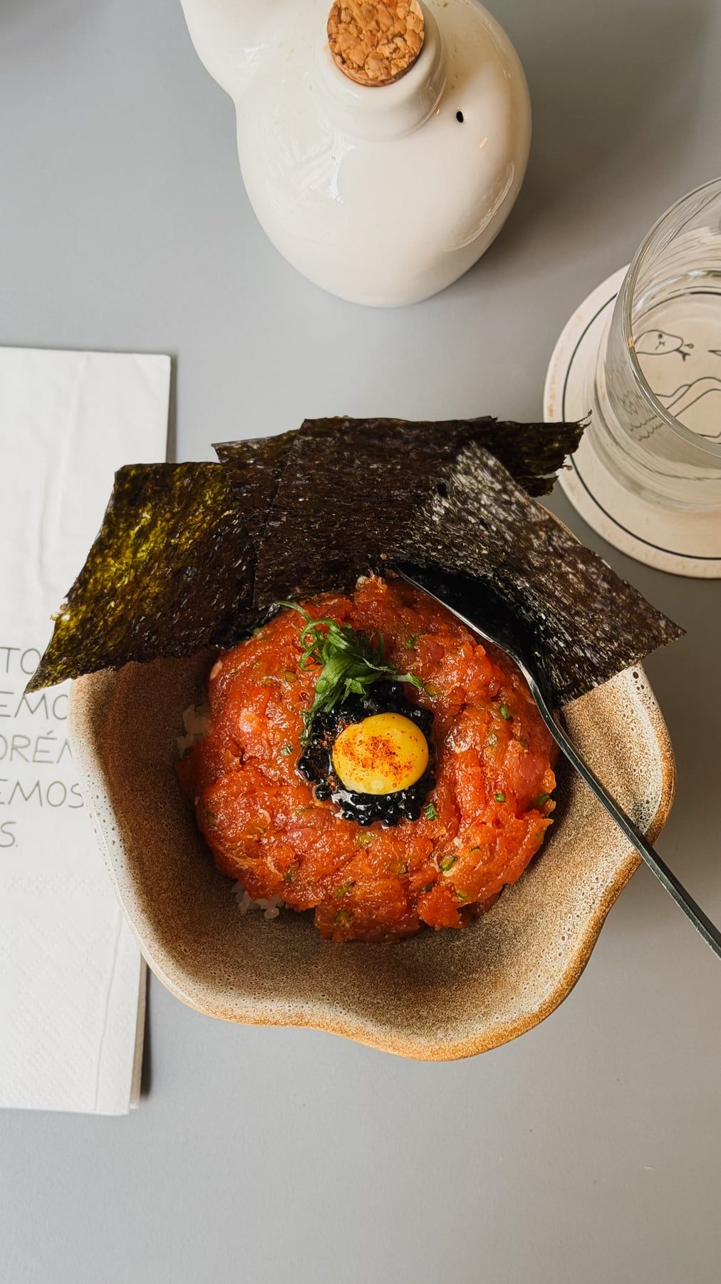 Tigela de cerâmica com tartare de peixe, uma gema no centro e uma folha de alga por cima.